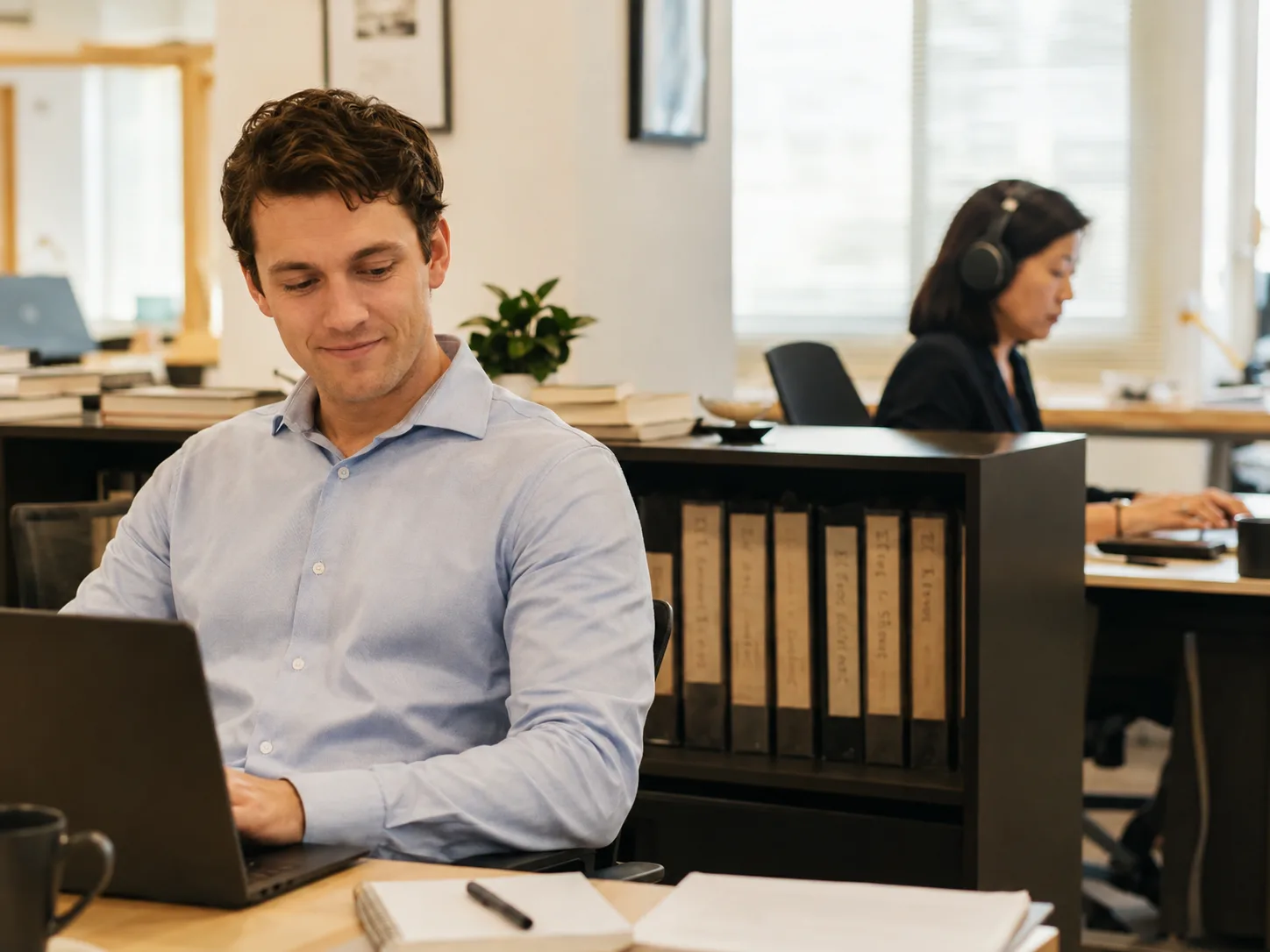 A young early-career professional getting an instant answer from the company knowledge base while a senior expert looks on, warm office light
